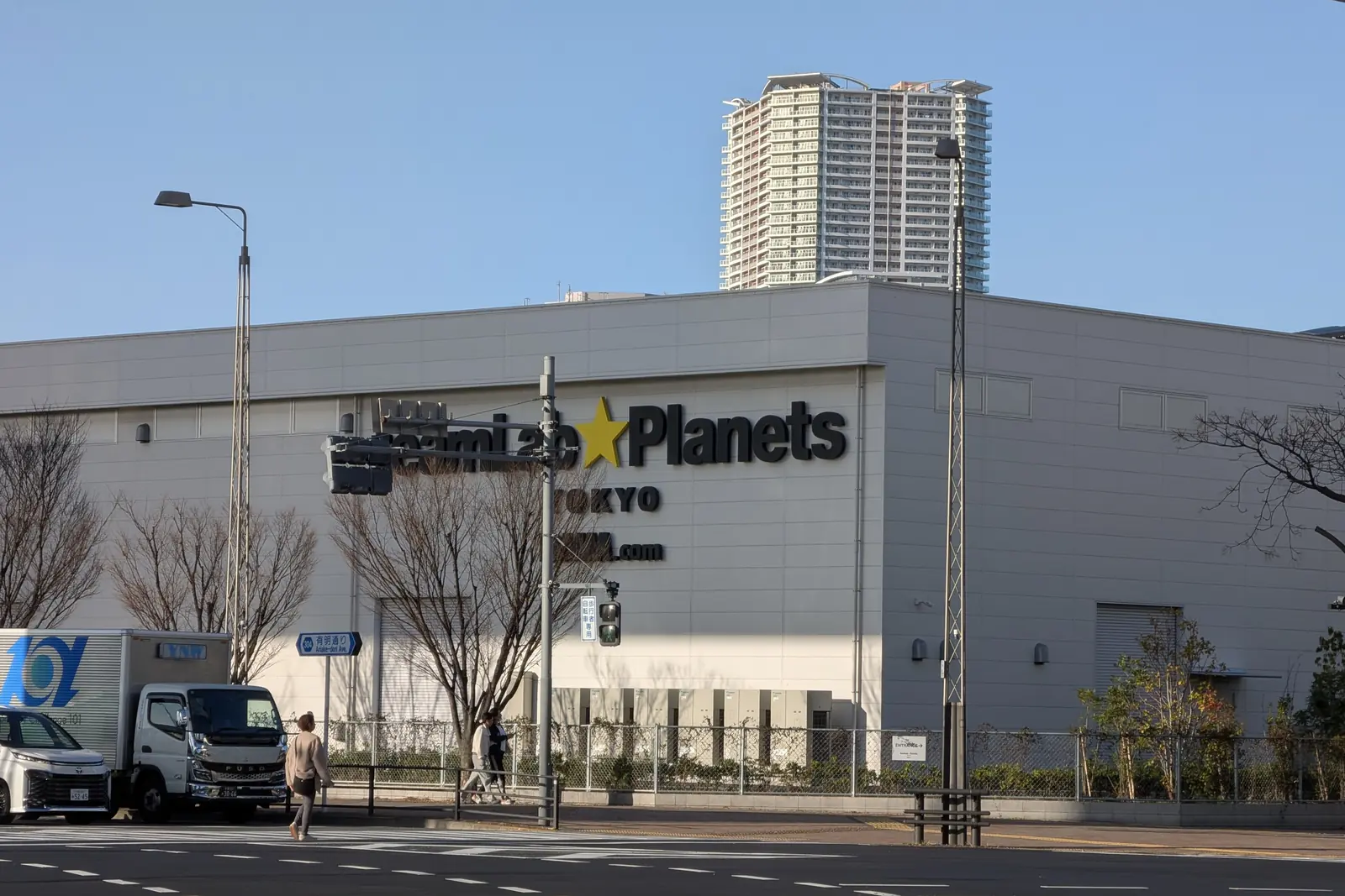 The grey exterior wall of the teamLab Planets building in Toyosu under a clear sky, with the museum's name on the facade and a pedestrian crossing in front; an exterior photograph, no artwork shown